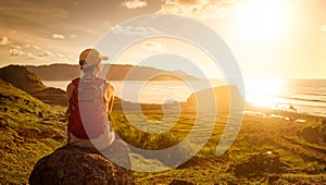 Young woman with backpack sitting on cliff and looking to a suns