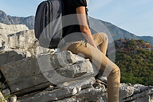 Young woman with backpack sitting on the edge of the mountain cliff against beautiful mountains peak