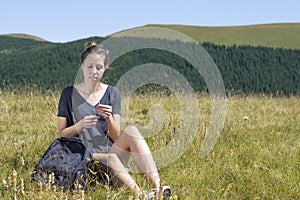 Young woman with backpack sitting in the field and golding a st