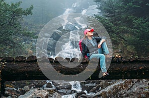 Young woman with backpack sitting on a wooden bridge and enjoying of power mountain river waterfall during Makalu Barun National