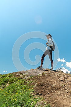 Young woman with backpack standing on cliff edge and looking to landscape. Hiking and travel in mountain