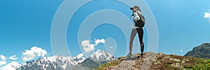 Young woman with backpack standing on cliff edge and looking to landscape