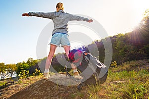 Young woman with backpack standing on cliff`s edge and looking t