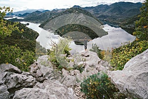 Young woman with backpack standing on cliff`s edge and looking t