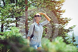 Young woman with backpack standing on cliff`s edge and looking to a sky