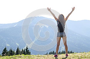 Young woman with backpack standing on cliff& x27;s edge and looking to a sky with raised hands, free space for your text.