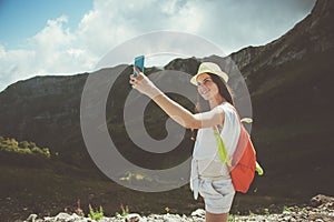 Young woman with backpack taking selfie photo with mobile phone. High mountains touristic path