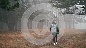 A young woman with a backpack walking along a path in the park to a misty forest