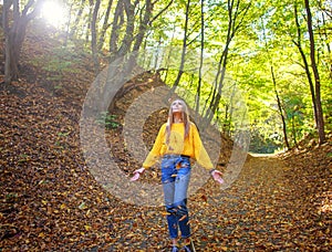 Young woman with backpack walks through the city forest park and enjoys nature on autumn sunny day