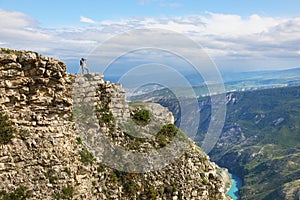 Young woman backpacker standing on cliff`s edge and taking a photo