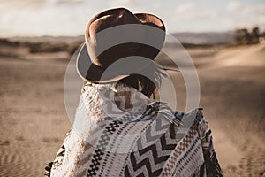 Young woman from backwards with scarf and hat in the desert at sunset