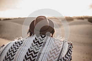 Young woman from backwards with scarf and hat in the desert at sunset