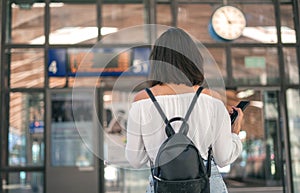Young woman with bag and backpack in the trainstation in front of timetables photo