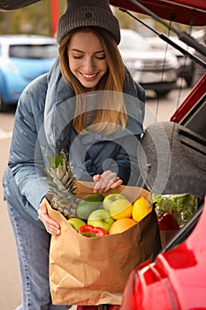 Young woman with bag of groceries near her car outdoors