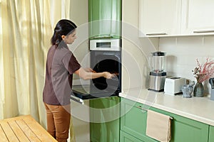 A young woman bakes in an oven that is ergonomically built in at chest level