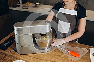 Young woman baking an apple pie in the kitchen standing at the counter in her apron using a handheld mixer to whisk the