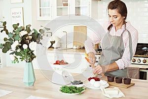 Young woman baking a cake in the kitchen standing at the counter in her apron using mixer to whisk