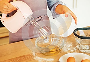 Young woman baking a cake in the kitchen, using a mixer to whisk the fresh ingredients in a glass mixing bowl.