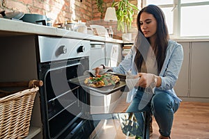 Young woman baking home pizza in kitchen at her home