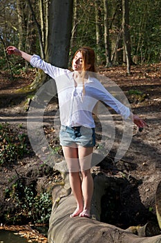 Young woman balancing on tree trunk with arms outstretched