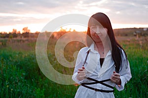 young woman in baldric on the summer field on sunset or sunrise. peaceful calm female. trendy clothes photo