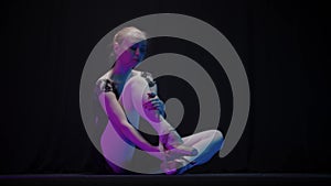 Young woman ballerina in black dress sits on the floor and takes off pointe shoes