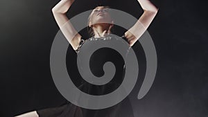 Young woman ballerina in black dress training her dancing in black studio