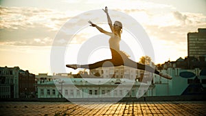 Young woman ballerina jump performing a split - bright sunset