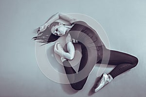 Young woman ballerina lying and stretching on the floor at ballet studio, view from above. Black and white.