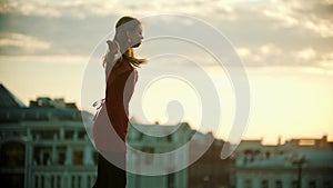 Young woman ballerina in red dress dancing on the roof - runs up and jump performing a split - bright sunset