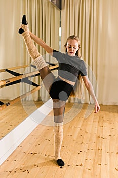 Young woman ballerina stretching and training at barre in dance studio - ballet and dancer concept