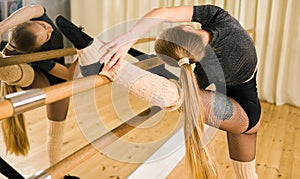Young woman ballerina stretching and training at barre in dance studio - ballet and dancer concept