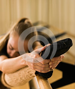 Young woman ballerina stretching and training at barre in dance studio close-up - ballet and dancer concept