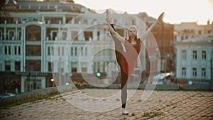 Young woman ballerina training on the roof - standing in the pose showing her stretching - sunset
