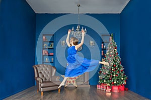 Young woman ballet dancer jumping in blue dress in a festive New Year`s interior