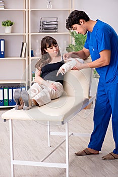 Young woman with bandaged arm visiting male doctor traumotologis