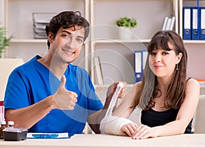 Young woman with bandaged arm visiting male doctor traumotologis