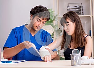 Young woman with bandaged arm visiting male doctor traumotologis