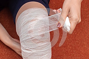 A young woman bandages a bandage on her injured knee. Top view. Self-help in case of a knee injury
