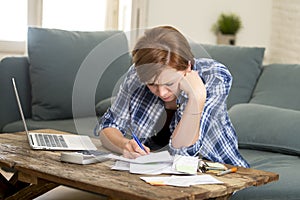 Young woman banking and accounting home monthly and credit card expenses with computer laptop doing paperwork with calculator