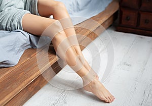 Young woman with bare legs closeup sitting on bed