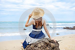 Young woman barefoot ware hat and sitting on stone see wave of sea water and sand on the beach