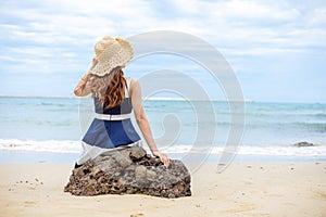 Young woman barefoot ware hat and sitting on stone see wave of sea water and sand on the beach