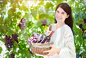 Young woman with a basket of grapes and bottles of wine at the vineyard