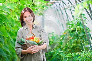 Young woman with basket of greenery and vegetables in the greenhouse. Harvesting time