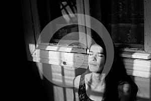 Young woman basking in the rays of the sun in the shadow of the window frames on the porch.