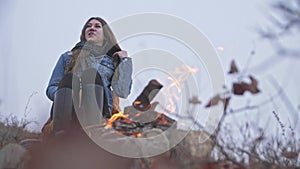 Young woman basks in the fire and says something in the autumn