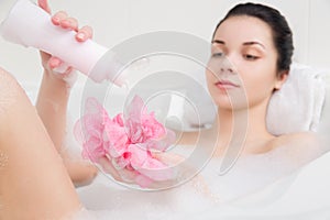 Young woman in a bath with foam sponge in hand