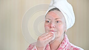 Young woman in bathrobe cleaning her face with cotton UHD