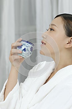 A young woman with a bathrobe enjoying tea